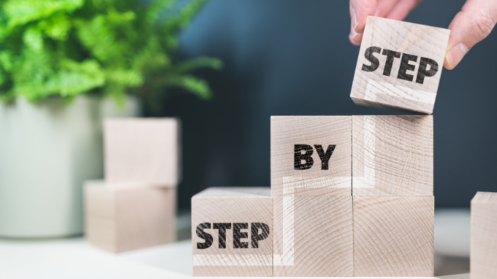 Image of wooden blocks creating steps and the words 'Step By Step' - we can get through the COVID-19 crisis in a step-by-step manner